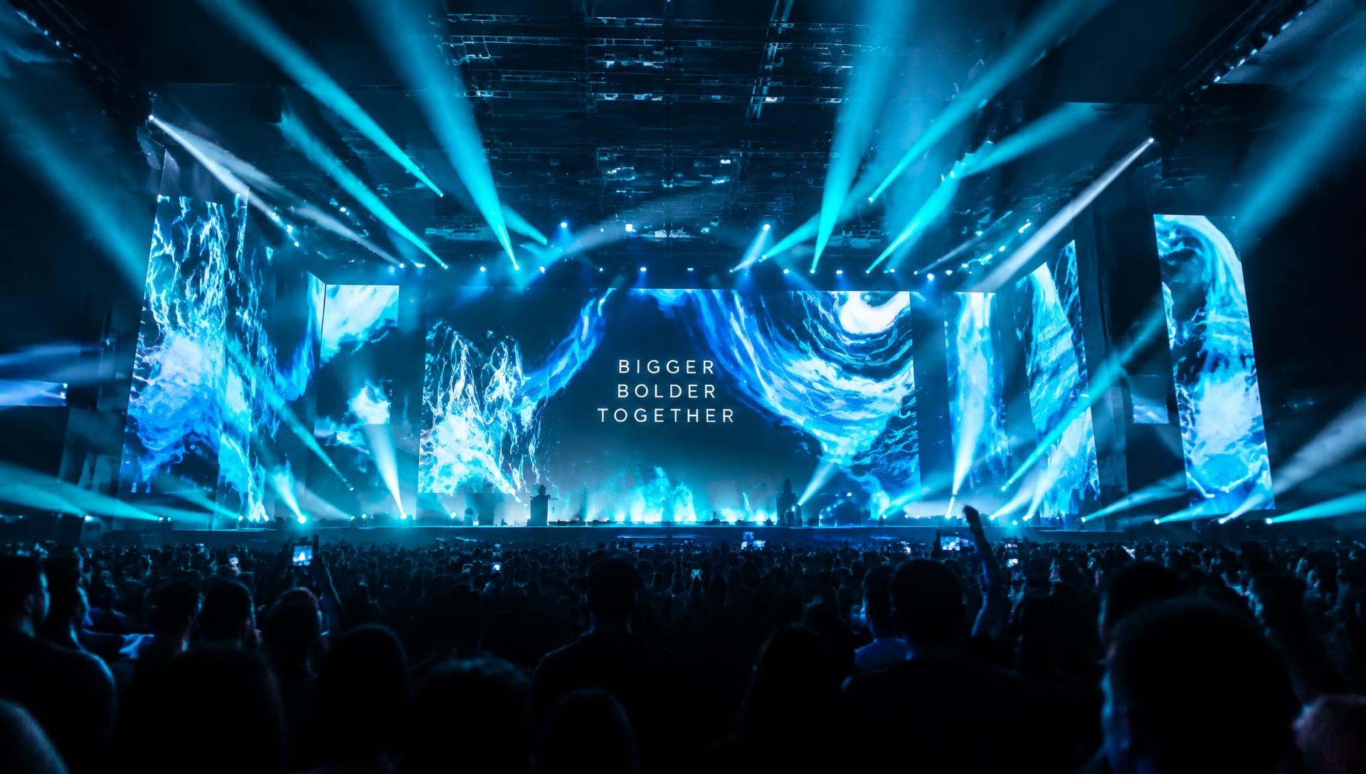 Crowded arena event with blue stage lighting and large LED screens